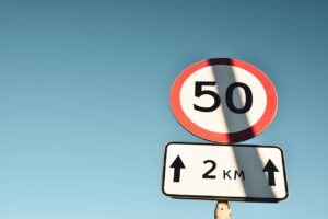 Clear speed limit and distance sign against blue sky, offering guidance and information.