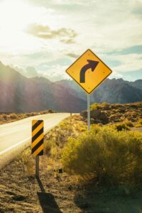 Empty highway with a right curve warning sign in a desert setting under sunny skies.